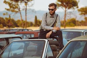 jung gut aussehend stilvoll Mann, tragen Hemd und Krawatte auf das Feld von alt Autos foto