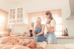 glücklich Lesben Paar halten Tassen von Kaffee im Küche. Paar von Lesben Mädchen genießen Kaffee beim Zuhause nehmen Über etwas. zwei jung Erwachsene schön Frauen trinken Tee im modern Küche. warm Ton. foto