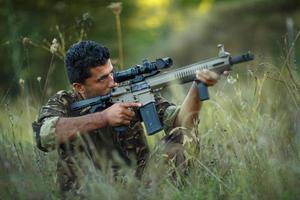 Mann von arabisch Staatsangehörigkeit im tarnen mit ein Gewehr Zielen beim ein Ziel foto