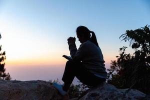 Nahansicht von ein jung asiatisch Frau beten, gegen abstrakt Sonnenaufgang Hintergrund. Silhouette von Frau kniend Nieder beten zum Anbetung Gott beim Himmel Hintergrund. Christen beten zu Jesus Christus zum Ruhe. foto