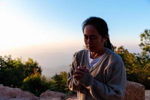 Nahansicht von ein jung asiatisch Frau beten, gegen abstrakt Sonnenaufgang Hintergrund. Silhouette von Frau kniend Nieder beten zum Anbetung Gott beim Himmel Hintergrund. Christen beten zu Jesus Christus zum Ruhe. foto