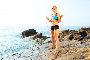 Athlet Frau tun Sport ausüben mit das Seil auf das Felsen durch das Meer foto