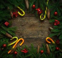 Weihnachtsgrenze mit Tannenzweigen, Zapfen, Weihnachtsschmuck und Zuckerstange auf rustikalen Holzbrettern foto