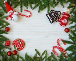 Weihnachten Rand mit Tanne Baum Geäst, Weihnachten Dekorationen und Süßigkeiten Stock auf Weiß hölzern Bretter foto