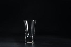 leeren Glas von Wodka auf schwarz Hintergrund. ein leeren trinken transparent Glas auf ein schwarz Hintergrund. isolieren. Kopieren Raum foto