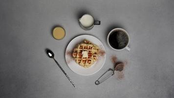 oben Aussicht von lecker Waffeln Platte, Karamell Soße, Kaffee Tasse, Milch, Dessertlöffel, Sieb auf ein grau Beton Hintergrund foto