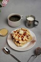 hausgemacht von lecker Waffeln Platte, Karamell Soße, Kaffee Tasse, Milch auf ein grau Hintergrund foto