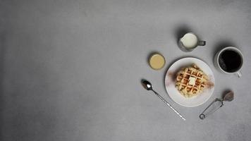oben Aussicht von lecker Waffeln Platte, Karamell Soße, Kaffee Tasse, Milch, Dessertlöffel, Sieb auf ein grau Beton Hintergrund foto