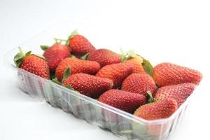 Erdbeeren in einem Plastikbehälter auf einem weißen Hintergrund foto