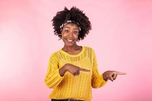 horizontal Schuss zufrieden dunkel gehäutet weiblich mit afro Haarschnitt, Punkte richtig mit beide Vordergrund Finger, zeigt an leer Raum zum Ihre Förderung, isoliert Über Rosa Hintergrund. Menschen, Werbung Konzept foto