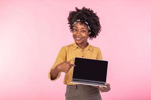 aufgeregt afrikanisch Mädchen halten Laptop mit schwarz Bildschirm. glücklich Geschäft Frau zeigen mit Finger auf das Bildschirm von Laptop. Werbung Konzept foto