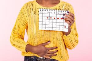 abgeschnitten Schuss Krankheit Frau halten Perioden Kalender zum Überprüfung Menstruation Tage stellen Hand auf Bauch isoliert auf Rosa Hintergrund. medizinisch, Gesundheitspflege, gynäkologisch Konzept. Kopieren Raum foto