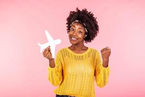 Foto von afrikanisch amerikanisch positiv süß ziemlich schön Mädchen gewonnen Tickets zu gehen im Ausland durch Luft Flugzeug Jubel aufgeregt Emotionen halten Flugzeug isoliert lockig wellig Rosa lebendig Farbe Hintergrund