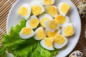 gekocht Eier Essen, Wachtel Eier auf Weiß Platte, Frühstück Eier mit frisch Wachtel Eier und Gemüse Grüner Salat Salat auf hölzern Tabelle Hintergrund foto