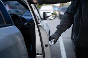 Nahansicht Schuss von ein Dieb tragen ein schwarz Hemd und schwarz Handschuhe. er versucht zu öffnen das Auto Tür und versucht zu brechen In. Auto Diebstahl Konzept. foto