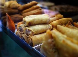 Stapel von tief gebraten Frühling Rollen und andere Essen angezeigt zum Verkauf im das Essen Geschäft im Spanien, Essen Kultur, Snack foto