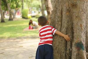 ein Junge versteckt sich hinter ein Baum damit seine Mutter kippen sehen foto