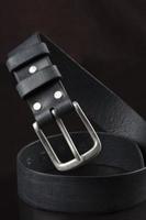 schwarzer Ledergürtel auf dunklem Hintergrund. Leder Produkte. foto
