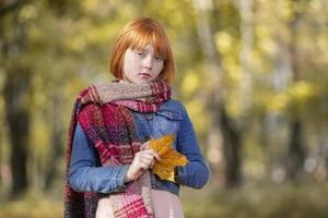 traurig nachdenklich rothaarig Mädchen mit ein Ahorn Blatt im das Herbst Park. foto