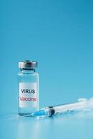 Ampulle und Spritze mit dem Impfstoff gegen das Virus gegen Krankheiten auf blauem Hintergrund. foto