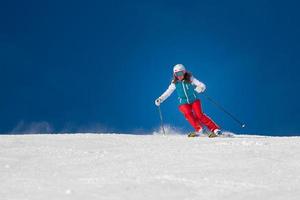 Skifahrerin, die an einem sonnigen Tag bergab fährt foto