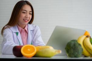 porträt einer asiatischen lächelnden ernährungsberaterin, die auf einem laptop-computer einen ausgewogenen korrekturdiätplan für patienten- oder gewichtsverlustratschläge tippt. konzept des gesunden lebensstils, der gesunden ernährung, der diät foto