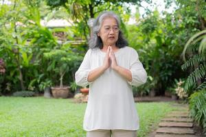 Porträt von ein asiatisch Senior Frau tun Yoga und Dehnen Übung im das Garten zum ein trainieren. Konzept von Lebensstil Fitness und gesund. asiatisch Frauen sind üben Yoga im Park. gesund Lebensstil foto