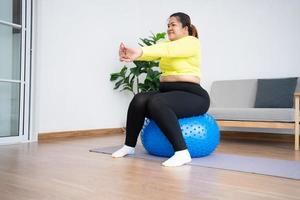 Portrait plus Größe Frau beim Training mit Fitnessball im Fitnessstudio zu Hause. übergewichtige frau, die auf einem pilatesball sitzt und ihre muskeln dehnt, bevor sie trainiert. gesundheitswesen und gewichtsverlustkonzept. foto