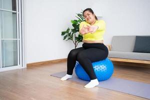 Portrait plus Größe Frau beim Training mit Fitnessball im Fitnessstudio zu Hause. übergewichtige frau, die auf einem pilatesball sitzt und ihre muskeln dehnt, bevor sie trainiert. gesundheitswesen und gewichtsverlustkonzept. foto