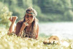 hübsches freies Hippie-Mädchen, das auf dem Gras raucht, Fotoeffekt des Weinleseeffekts foto