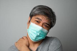 Kranker asiatischer Mann mit medizinischer Gesichtsmaske und Schulterschmerzen und Stress. konzept des schutzes pandemie coronavirus und atemwegserkrankungen foto