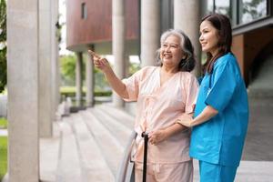 asiatisch Vorsichtig Pflegekraft oder Krankenschwester halt geduldig Hand und ermutigen geduldig, Gehen im Garten. Konzept von glücklich Pensionierung mit Pflege von ein Pflegekraft und Ersparnisse und Senior Gesundheit Versicherung. foto