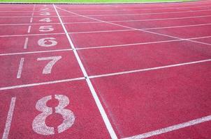 Zahlen beginnend Punkt auf rot Laufen verfolgen, laufen Spur und Grün Gras, direkt Leichtathletik Laufen Spur beim Sport Stadion foto