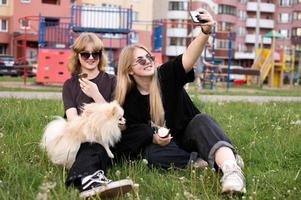 zwei komisch Mädchen sind Essen Eis Sahne und spielen mit ein pommerschen Hund. nehmen Selfies foto