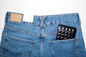 ein Paar von Neu Blau Denim Hose mit ein leeren Leder Etikett, ein schwarz Brieftasche im das zurück Tasche. foto