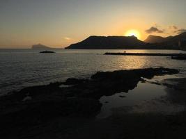 Mittelmeerstrand ohne Menschen bei Sonnenuntergang in Calpe, Alicante foto