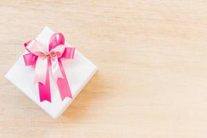 rosa Bandschleife auf einer weißen Geschenkbox auf einem hölzernen Hintergrund foto