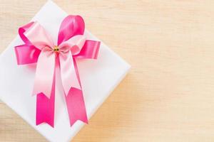 rosa Bandschleife auf einer weißen Geschenkbox auf einem hölzernen Hintergrund foto