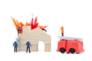 Miniatur-Feuerwehrleute, die sich um einen Brand in einem Holzhaus kümmern foto