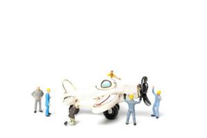Miniaturarbeiter, die ein Spielzeugflugzeug auf einem weißen Hintergrund reparieren foto