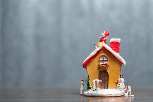 Miniaturmenschen, die ein Haus und einen Weihnachtsmann malen, die auf dem Dach sitzen, frohe Weihnachten und frohe Feiertagskonzept