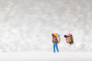Miniatur-Rucksacktouristen, die auf einem Schneehintergrund, Winterkonzept gehen