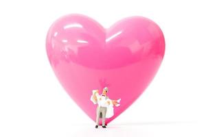 Miniaturpaar mit einem rosa Herzen auf einem weißen Hintergrund, Valentinstagskonzept foto