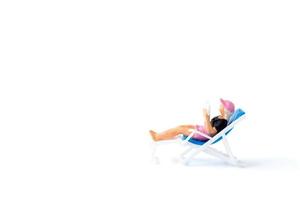 Miniaturperson, die sich auf einem Liegestuhl auf einem weißen Hintergrund sonnt, Sommerkonzept foto