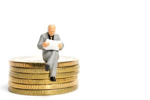 Miniaturgeschäftsmann, der auf einem Stapel von Münzen, Geld und Finanzkonzept sitzt foto