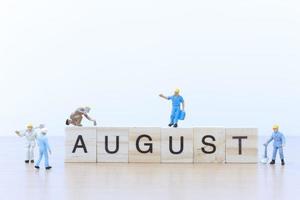 Miniaturmenschen, die an Holzklötzen mit dem Wort August auf einem Holzboden arbeiten foto