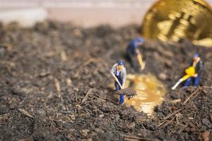Miniaturarbeiter graben den Boden, um glänzende Bitcoin-Kryptowährung aufzudecken, erfolgreiches Arbeitskonzept foto