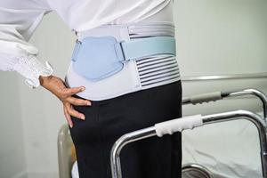 asiatische Patientin mit Rückenschmerzen-Unterstützungsgurt für orthopädische Lendenwirbelsäule mit Gehhilfe. foto