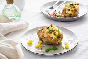 zweimal gebacken Kartoffeln im ihr Skins mit Käse und Speck Krümel auf Platten auf ein hölzern Tisch. Flexitarier Diät foto