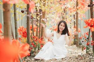 asiatische Frau in einem weißen Kleid, das Blätter wirft, während sie im Park sitzt foto